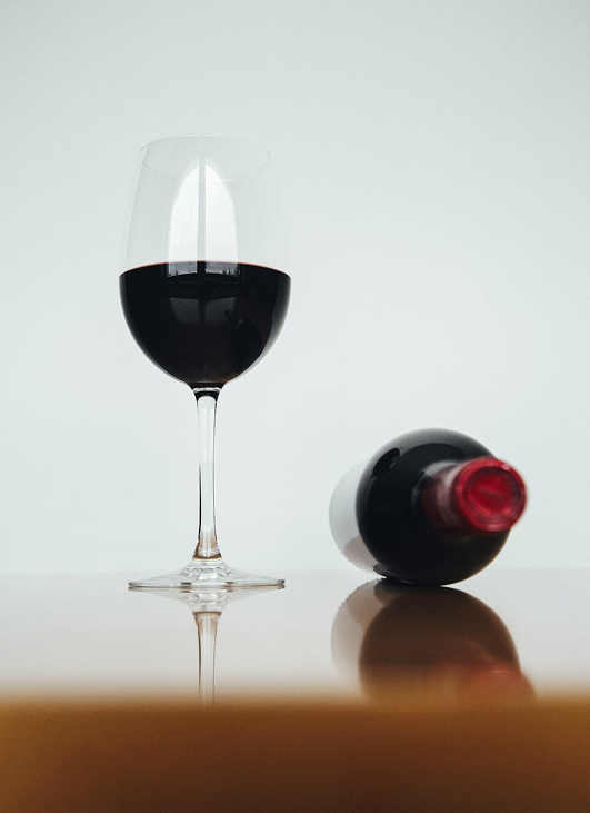 Una copa de vino tinto junto a una botella de vino.